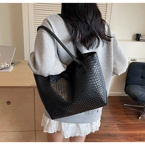 Detail of a large black tote bag with woven texture worn by a model in a modern room