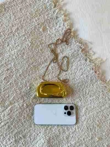 Detailed top view of a mini gold metallic chain bag shown next to a smartphone for scale
