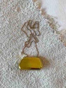Detailed macro view of the gold mirror finish and thin metal chain of this evening clutch