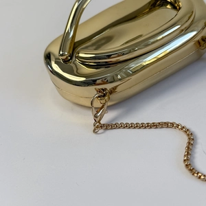 Close-up of golden evening clutch with smooth metal finish and detachable chain link