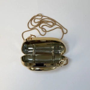 Detail of gold oval capsule clutch showing polished mirror finish and chain strap