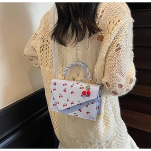 Détail du sac à main bleu clair avec imprimé cerises, poignée tressée et charm