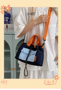Detail of navy canvas tote bag featuring light blue front pocket and bright orange handles