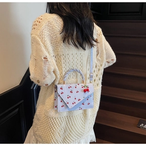 Détail du sac bandoulière bleu clair à motifs cerises et poignée tissée sur mannequin