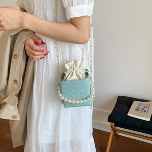 Mint green box bag with pearl handle and gold chain strap shown on model in soft light