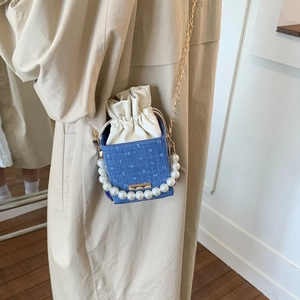 Blauwe denim emmertas met parelhandvat en gouden ketting op een stijlvolle beige jas