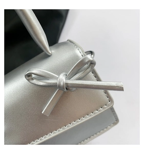 Detail of silver metallic square bag with a handcrafted leather bow and neat stitching