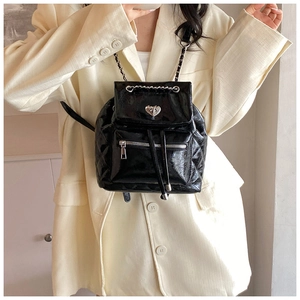 Classic black quilted backpack with silver chain straps worn on a beige blazer