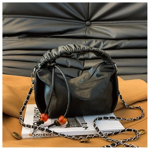 Détail d'un sac plissé noir avec texture florale et perles d'ambre orange décoratives