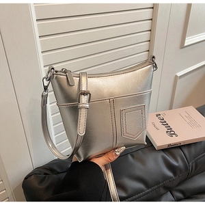 Detail der silbernen Metallic-Eimertasche mit braunen Kontrastnähten und Schultergurt