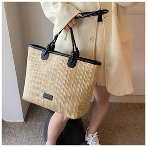 Close-up of woven straw tote bag with black leather trim and handles for summer vacation