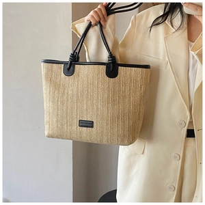Detail of woven straw tote bag with black faux leather straps and decorative knots