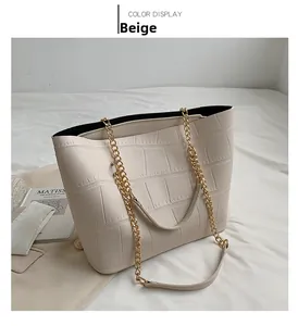 Close-up of beige tote bag with crocodile texture and gold metal chain strap detail