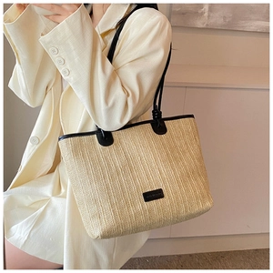 Close-up of woven straw tote bag featuring contrast black leather handles and trim