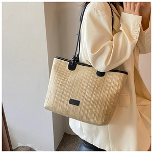 Detail of woven straw tote bag featuring black leather trim and fine shoulder straps