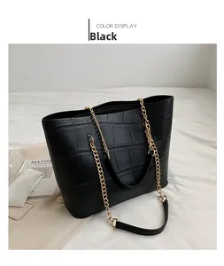 Macro detail of black crocodile embossed tote bag with gold chain strap on white fabric