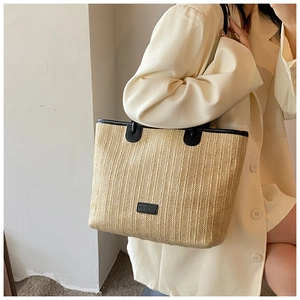 Detail of woven straw tote bag with black faux leather straps worn by model on shoulder