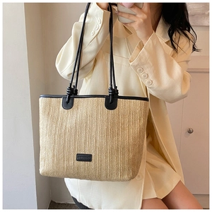 Detail of woven straw tote bag with black leather trim and logo patch on the side