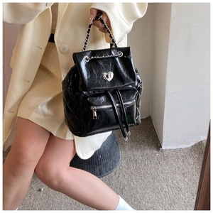 On-body shot of a black patent leather backpack with silver heart buckle and chain strap