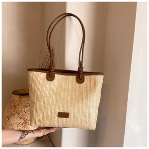 Close-up of woven straw tote bag featuring brown leather straps and knotted detail