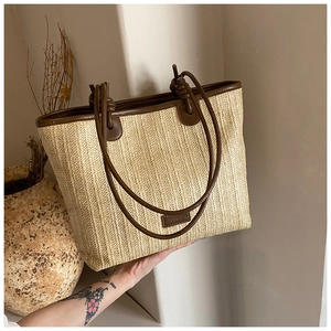 Detail of woven straw tote bag featuring brown leather straps and knotted accents