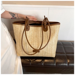 Close-up of woven straw tote bag with brown leather handles and knot detail on a bench