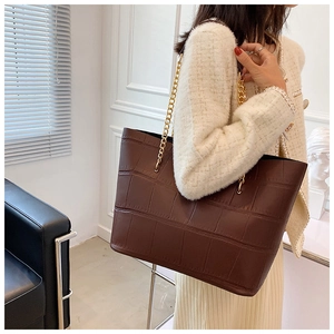 Detail of dark brown tote bag with crocodile texture and gold chain shoulder strap