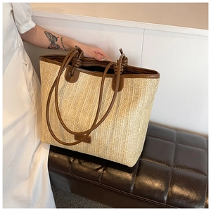 Detail of woven straw tote bag with brown leather handles and decorative knot detail