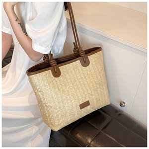 Close-up of a minimalist woven straw tote bag with brown leather handles and logo detail