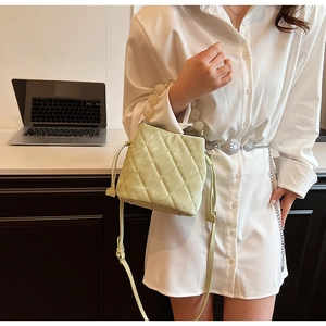 Détail d'un sac seau matelassé vert clair avec anse en perles et bandoulière sur un bureau