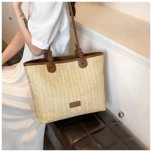 Close-up of woven straw tote bag with brown leather handles and brand label detail
