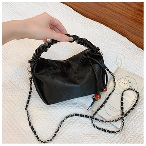 Détail d'un sac à main noir plissé avec texture satinée, perles d'ambre et bandoulière