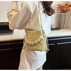 Sac seau matelassé vert pâle avec poignée en perles et cordon, porté en bandoulière
