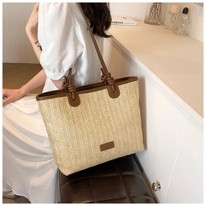 Detail of a large woven straw tote bag with brown leather straps and knot accents