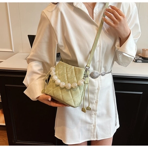 Détail du sac seau matelassé vert clair avec une poignée décorative en perles