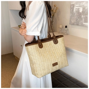 Close-up detail of woven straw tote bag with brown leather handles and knot accents
