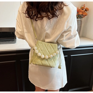 Détail d'un sac seau matelassé vert clair avec anse en perles porté à l'épaule