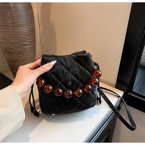 Détails du sac seau en velours noir avec motif matelassé et poignée en perles ambre
