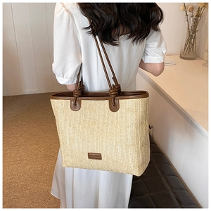 Detail of hand-woven straw tote bag featuring brown PU leather straps and a logo patch