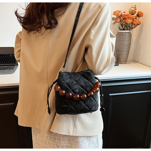 Détail du sac seau noir matelassé avec perles ambrées et pieds de protection