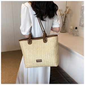 Detail of woven straw tote bag featuring brown leather trim and shoulder straps