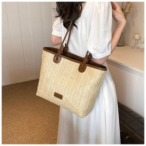 Detail of beige straw tote bag with brown leather straps and knot accents on shoulder