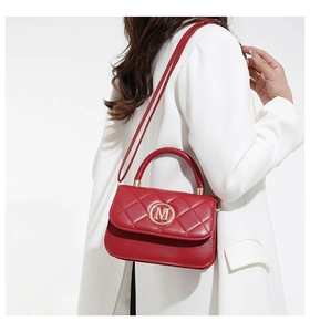 Detail of red quilted leather bag with M metal logo and gold handle on white coat