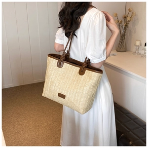 Detail of hand-woven straw tote bag with brown leather handles for summer vacation