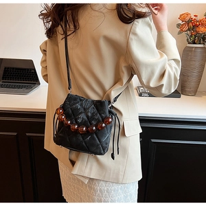 Détail du sac seau matelassé noir avec chaîne en perles ambrées et fermeture à cordon