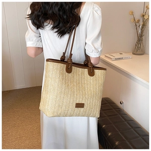 Detail of hand-woven straw tote with brown leather knotted handles and embossed logo patch