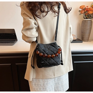 Vue détaillée du sac seau noir matelassé avec poignée en perles ambre et bandoulière cuir