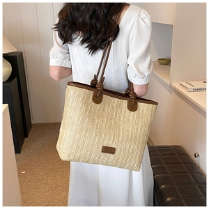 Close-up of woven straw tote bag featuring brown leather trim and knotted strap detail