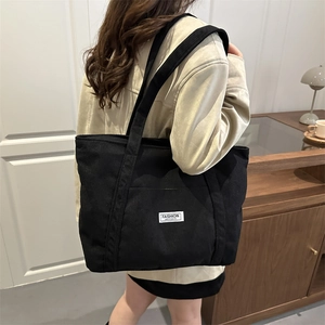 Black corduroy tote bag with dual shoulder straps and a front pocket for women