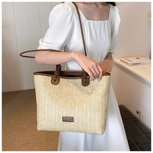 Close-up of beige straw tote bag with brown leather straps and metal logo detail